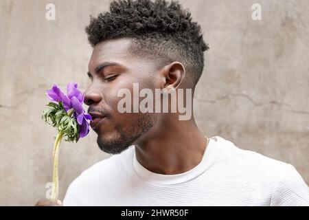 Junger Mann riecht vor der Wand nach purpurner Blume Stockfoto