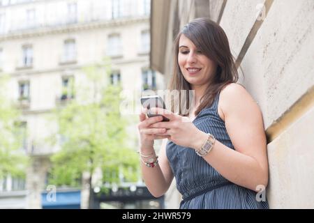 Junge Frau, die ein Mobiltelefon an der Wand benutzt Stockfoto