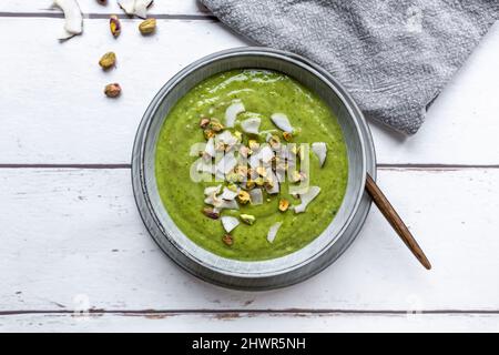 Studioaufnahme einer Schüssel mit veganer Erbsensuppe mit Zucchini, Brokkoli, Pistazien und Kokosnussfetzen Stockfoto