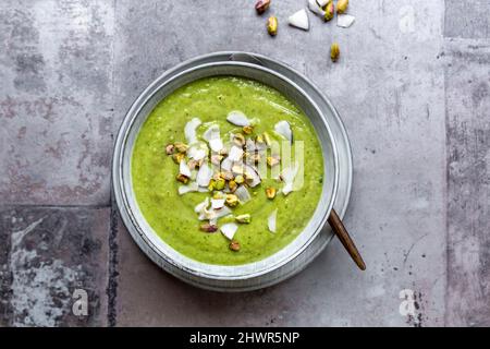 Studioaufnahme einer Schüssel mit veganer Erbsensuppe mit Zucchini, Brokkoli, Pistazien und Kokosnussfetzen Stockfoto