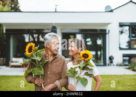 Glückliches Paar mit Sonnenblumen, die sich im Garten anguckten Stockfoto
