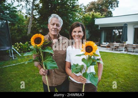Lächelnder Mann und Frau halten Sonnenblumen im Garten Stockfoto