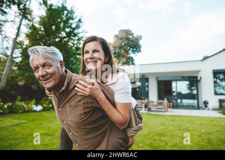 Glückliche Frau genießt Huckepack Fahrt von älteren Mann im Hinterhof gegeben Stockfoto