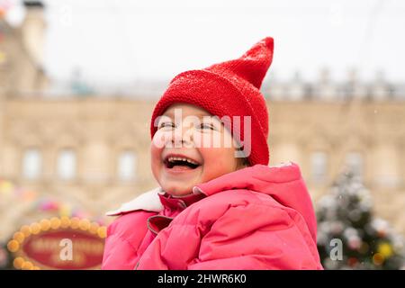 Fröhliches Mädchen trägt roten Strickmütze genießen auf dem Weihnachtsmarkt Stockfoto