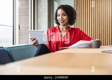Junge Geschäftsfrau mit Tablet-Computer und Kaffee auf dem Schreibtisch am Arbeitsplatz Stockfoto