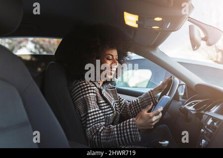 Fröhliche Frau mit Smartphone im Auto Stockfoto