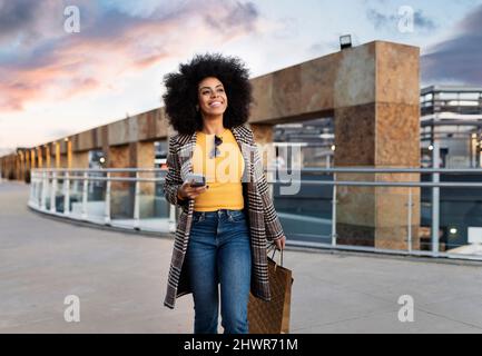 Lächelnde Frau mit Einkaufstaschen auf dem Fußweg Stockfoto