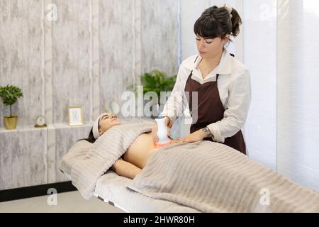 Therapeut, der Frau mit Werkzeug in der ästhetischen Klinik massiert Stockfoto