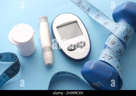 Nahaufnahme von Messgeräten für Diabetiker und blauer Hantel-Hintergrund Stockfoto