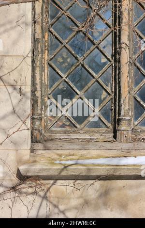 Altes gotisches mittelalterliches Fenster mit Scheiben in einem diagonalen Rahmen. Stockfoto