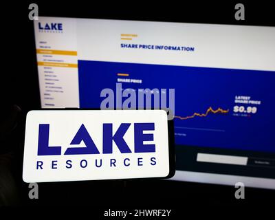 Person mit Mobiltelefon und Logo des australischen Lithiumunternehmens Lake Resources N.L. auf dem Bildschirm vor der Webseite. Konzentrieren Sie sich auf die Telefonanzeige. Stockfoto