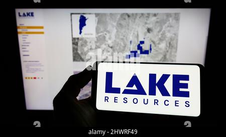 Person, die das Smartphone mit dem Logo des australischen Lithiumunternehmens Lake Resources N.L. auf dem Bildschirm vor der Website hält. Konzentrieren Sie sich auf die Telefonanzeige. Stockfoto
