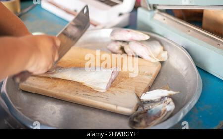 Der Koch schneidet getrocknetes Fischfilet auf einem Holzbrett in Stücke und bereitet die Zutaten für das Kochen in der Küche zu. Stockfoto