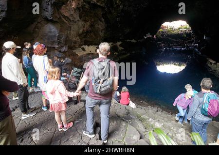 Touristen sitzen am Rand des Lavatunnels mit Salzwasser-Lagunen-See in jameos del agua lanzarote, kanarische Inseln, spanien die weißen Flecken sind die einzigartigen blin Stockfoto