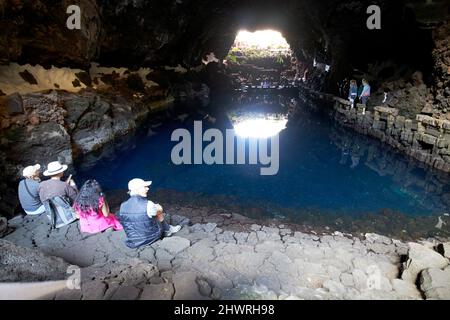 Touristen sitzen am Rand des Lavatunnels mit Salzwasser-Lagunen-See in jameos del agua lanzarote, kanarische Inseln, spanien die weißen Flecken sind die einzigartigen blin Stockfoto