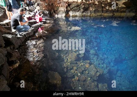 Touristen sitzen am Rand des Lavatunnels mit Salzwasser-Lagunen-See in jameos del agua lanzarote, kanarische Inseln, spanien die weißen Flecken sind die einzigartigen blin Stockfoto