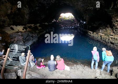 Touristen sitzen am Rand des Lavatunnels mit Salzwasser-Lagunen-See in jameos del agua lanzarote, kanarische Inseln, spanien die weißen Flecken sind die einzigartigen blin Stockfoto