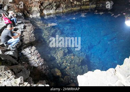 Touristen sitzen am Rand des Lavatunnels mit Salzwasser-Lagunen-See in jameos del agua lanzarote, kanarische Inseln, spanien die weißen Flecken sind die einzigartigen blin Stockfoto