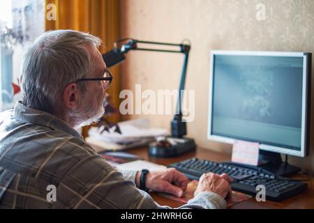 Ein älterer Mann, über 70, arbeitet zu Hause an einem Computer Stockfoto