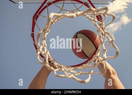 Guy dunking Basketball Ball durch Netzring mit Händen, Ziel Stockfoto