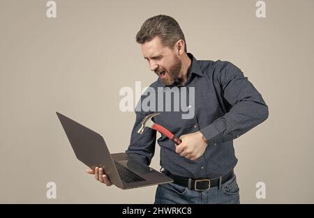 Wütender Mann schlug Laptop-Computer mit Hammer grauen Hintergrund, Absturz Stockfoto