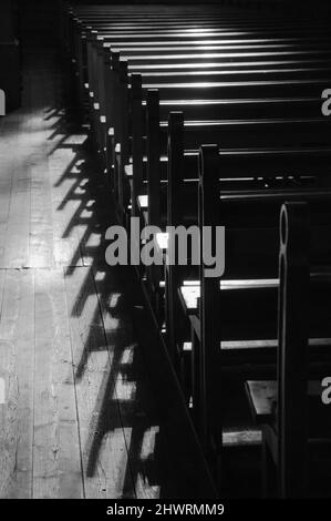 Reihen von Kirchenbänken. Sonnenlicht filterte durch das Buntglasfenster. Selektiver Fokus. Historisches Foto in Schwarzweiß. Stockfoto