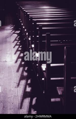 Reihen von Kirchenbänken. Sonnenlicht filterte durch das Buntglasfenster. Selektiver Fokus. Moody Veilchen traurig Stockfoto