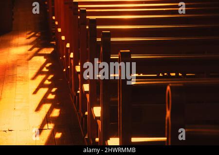 Reihen von Kirchenbänken. Sonnenlicht filterte durch das Buntglasfenster. Selektiver Fokus. Stockfoto