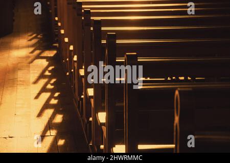 Reihen von Kirchenbänken. Sonnenlicht filterte durch das Buntglasfenster. Selektiver Fokus. Historisches Foto in Schwarzweiß Stockfoto