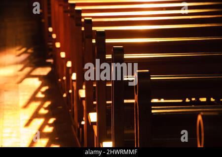 Reihen von Kirchenbänken. Sonnenlicht filterte durch das Buntglasfenster. Selektiver Fokus. Stockfoto