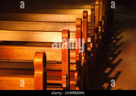 Reihen von Kirchenbänken. Sonnenlicht filterte durch das Buntglasfenster. Selektiver Fokus. Stockfoto