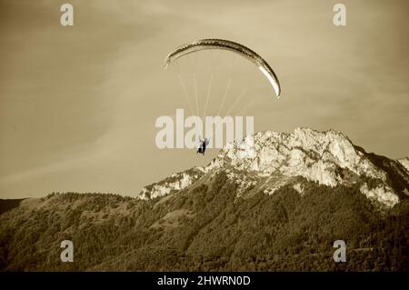 Gleitschirme fliegen im Tandem und Berge von Savoyen im Hintergrund. Annecy Lake, Frankreich. Sepia historisches Foto. Stockfoto