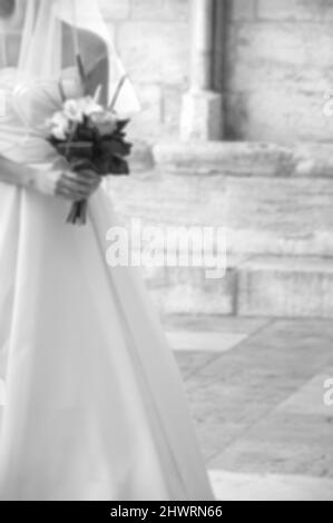 Verschwommenes Foto einer Braut, die an ihrem Hochzeitstag in die gotische Kirche eintrat. Schwarz und Weiß. Stockfoto