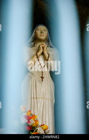 Statue der betenden Madonna in der Grotte Notre Dame des Sees in der Nähe des Sees von Annecy, die durch den Schmiedezaun gesehen wird. Duingt, Frankreich Stockfoto