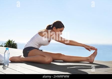 Machen Sie sich bereit für ihr Workout. Eine junge Frau, die sich vor dem Training auf dem Pier ausdehnt. Stockfoto