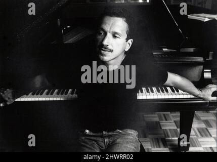 Ein 1982 geposiertes Porträt des Jazzpianisten Keith Jarrett in seinem Garagenstudio, dessen Arme über einem Flügel liegen. Stockfoto