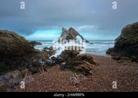 Herrlicher Blick auf die Klippen des Meeres, in Form eines Bogens und Steine im Vordergrund. Berühmte Felsformation an der Moray Coast, Schottische Highlands, Schottland. Bow Fiddle Rock. Stockfoto