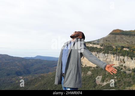 Ein Mann mit schwarzer Haut, die die Arme ausstreckt, feiert im Winter im Berg Stockfoto