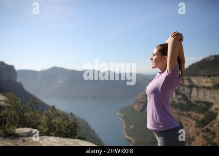 Seitenansicht Porträt einer Sportlerin, die die Arme in einer wunderschönen Landschaft streckt Stockfoto