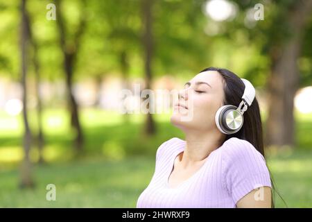 Entspannte asiatische Frau hört Musik sititng in einem grünen Park Stockfoto