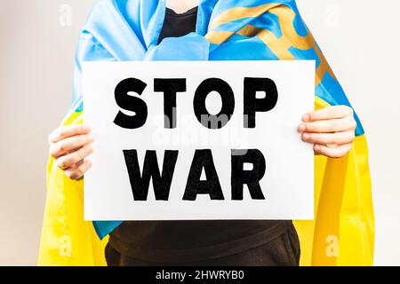 Der mit ukrainischer Flagge gewickelte Protestler hält ein Demonstrationsschild mit der Botschaft „Stop war“. Protest gegen Russland Angriff auf die Ukraine Stockfoto
