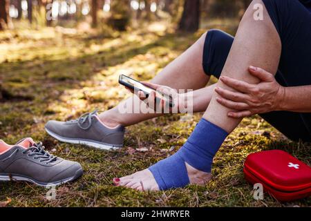 Verletzte Wanderer mit Verstauchung Knöchel mit Smartphone Hilfe zu bekommen. Frau gab sich erste Hilfe bei Wanderverletzungen in der Natur Stockfoto