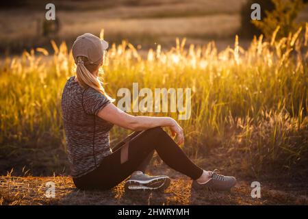 Laufin ruht sich nach dem Joggen im Freien aus. Frau, die nach dem Training eine Pause einnahm. Fitness aktiver Lebensstil Stockfoto