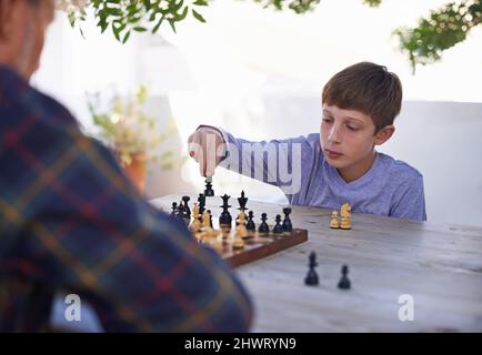 Sein Großvater ist ein würdiger Gegner. Aufnahme eines Jungen, der mit seinem Großvater Schach spielt. Stockfoto