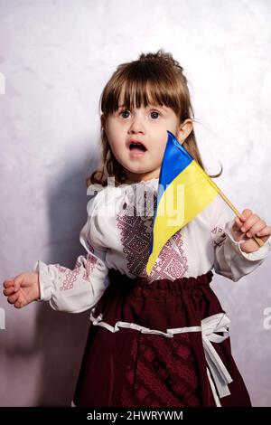 Baby Girl Ukrainisch in Stickkleid Protest gegen Kriegskonflikt wirft nationale Flagge Stockfoto