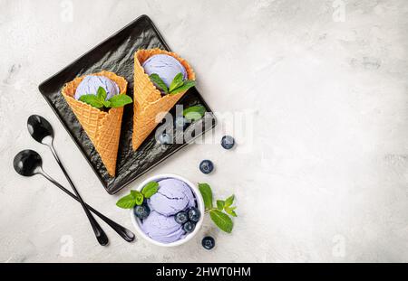 Heidelbeer-Eis in Waffelkegel auf schwarzem Teller auf grauem Hintergrund. Draufsicht, Kopierbereich. Stockfoto