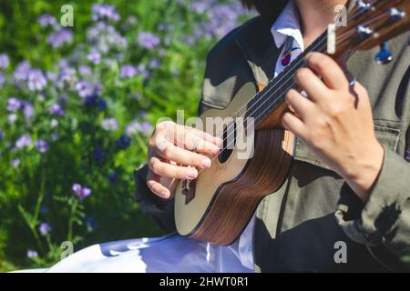 Frau, die im Freien Ukulele spielt. Musikerin spielt im Frühling gerne ein akustisches Instrument Stockfoto