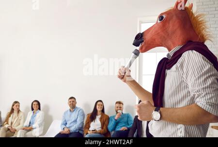 Business Speaker in Pferdemaske macht lustige Präsentation vor glücklichen Publikum Stockfoto