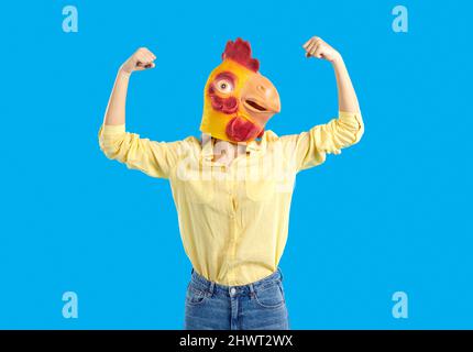 Junge Frau trägt eine lustige Hühnermaske, die sich stark vorgibt und ihre Arme beugt Stockfoto
