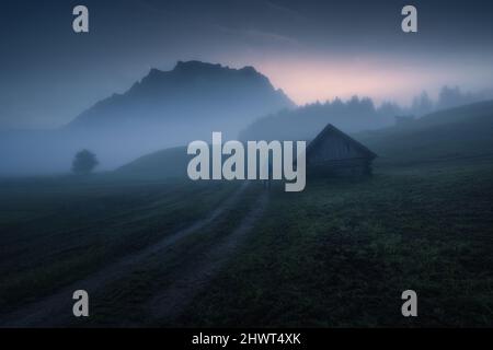 Nebliger Morgen mit einer Hütte und Bergen im Hintergrund Stockfoto